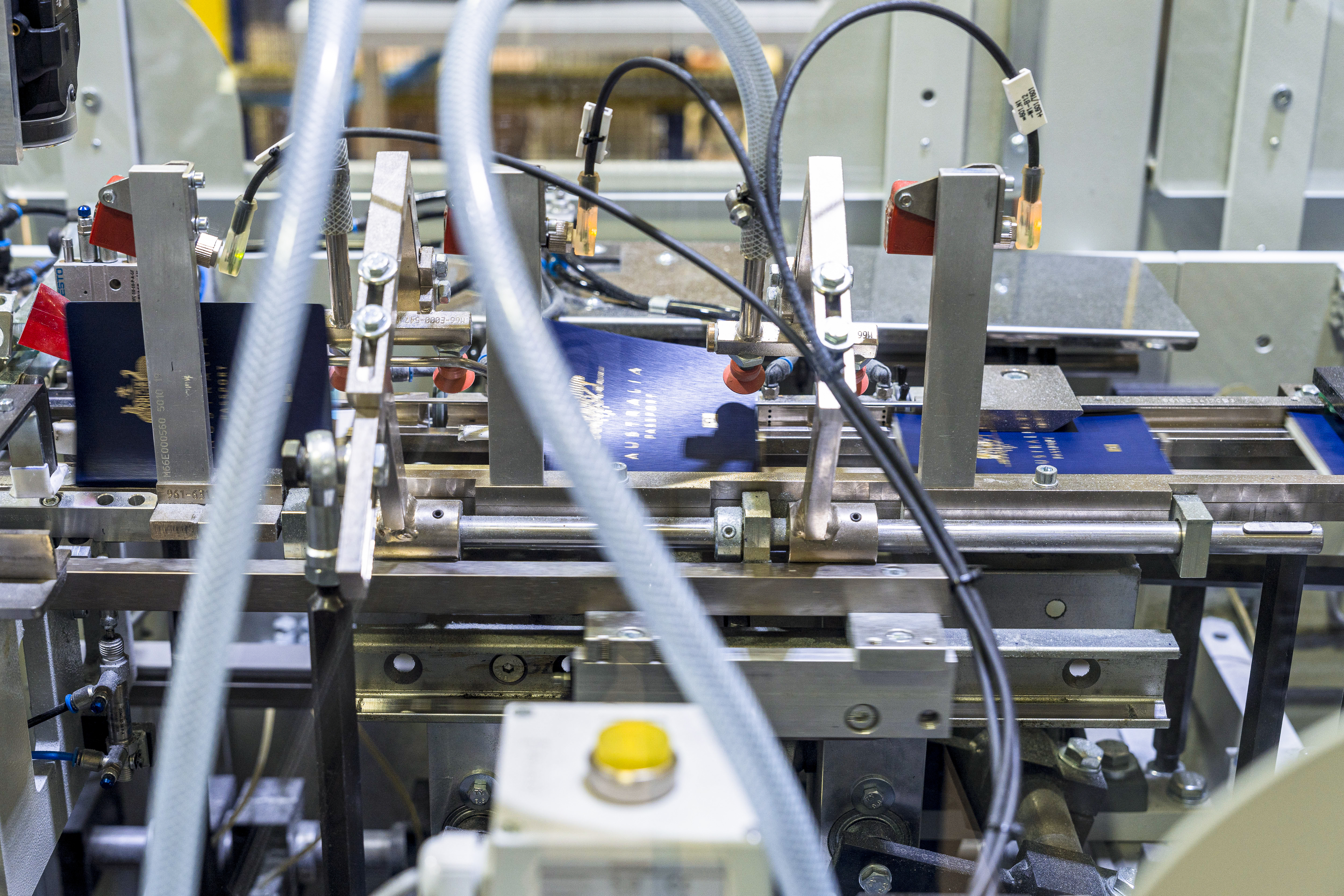 Two Australian passports making their way along the passport production line. The passports are in the centre of the image and surrounded by complex machinery.