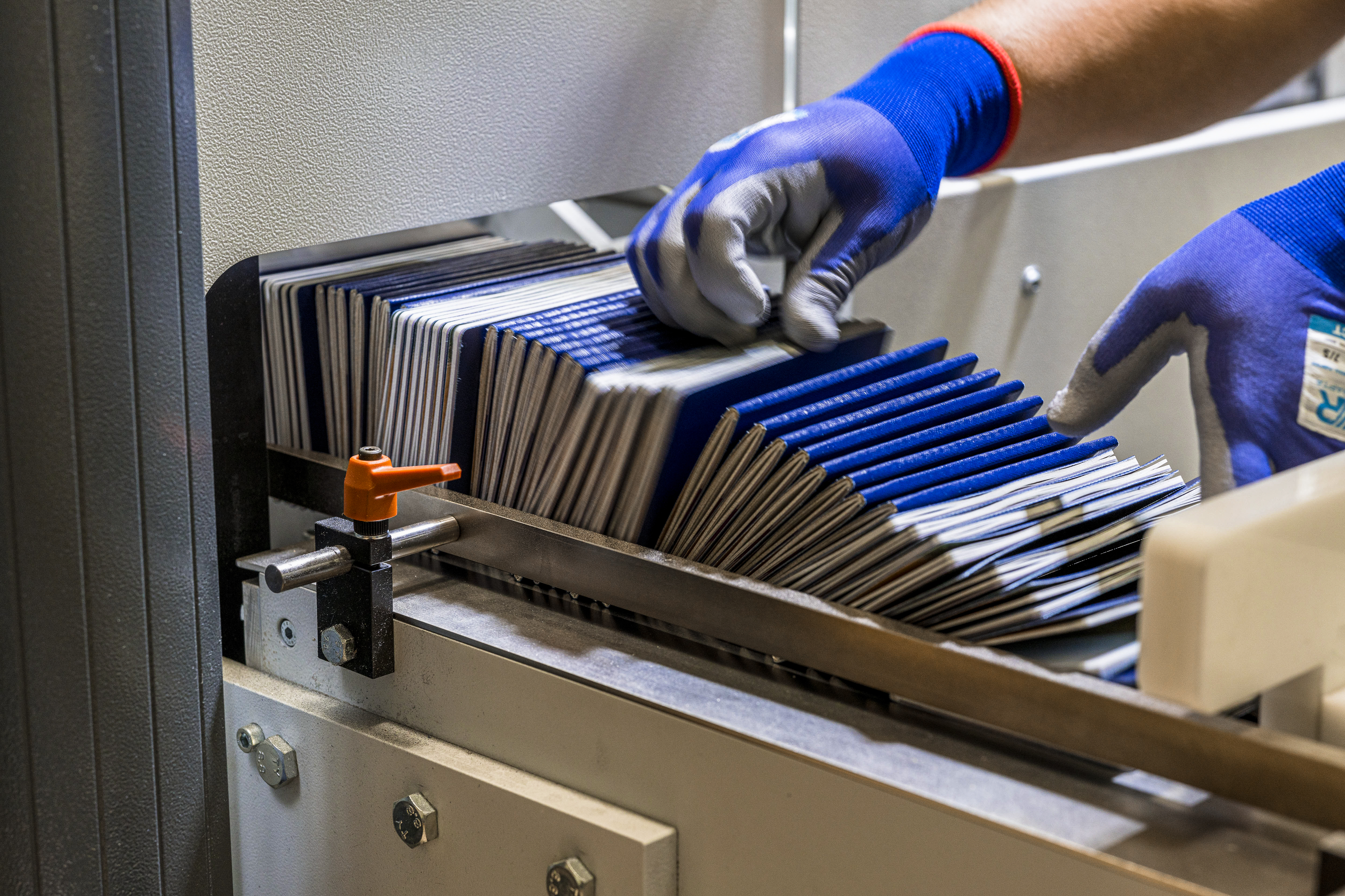Dozens of newly printed passports stacked side by side at the end of the production. A hand and a thumb from another hand can be seen about to transfer the new passports away.