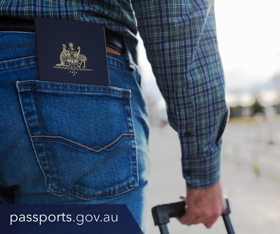 On the left side an Australian passport is showing out the top of a man's back jeans pocket. On the right his arm can be seen with his hand around the handle of a wheeled suitcase. 